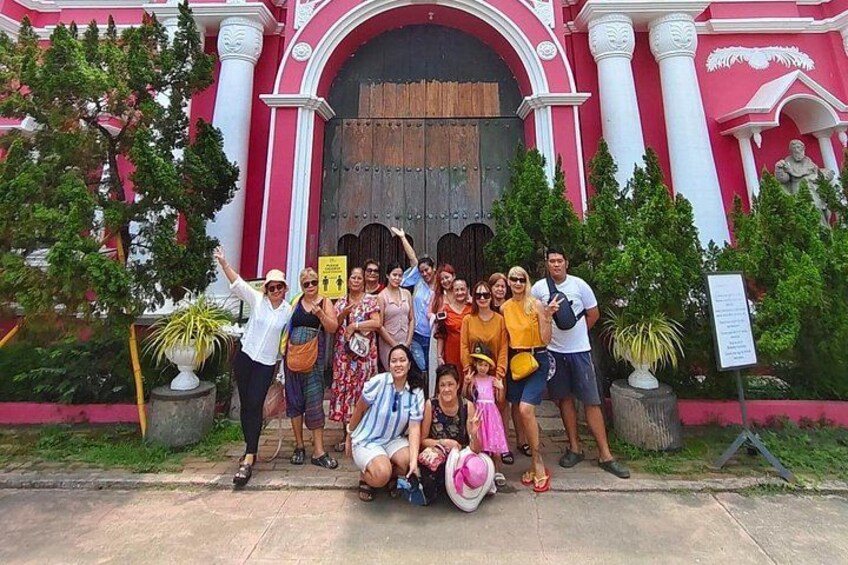 A group of people posing in front of a pink and white building with a large wooden door. 1