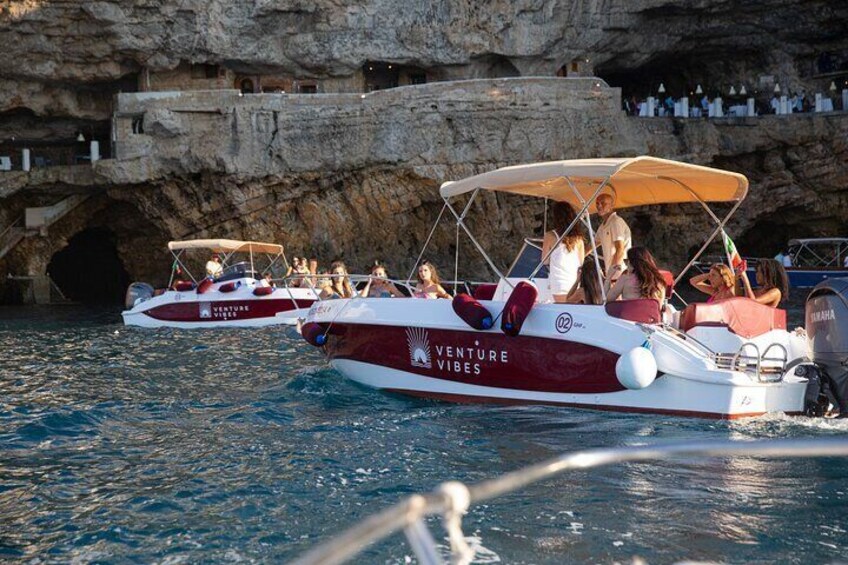 Deux bateaux, nommés « Venture Vibes », naviguent sur une eau calme, près d’une falaise rocheuse dont l’entrée d’une grotte est visible. 5