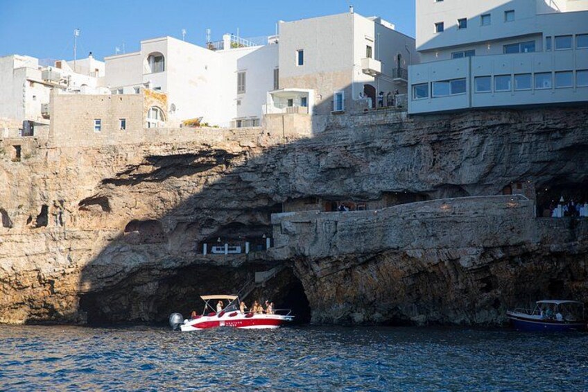 A coastal town with buildings on a cliff, a boat in the water, and a rocky outcrop. 5