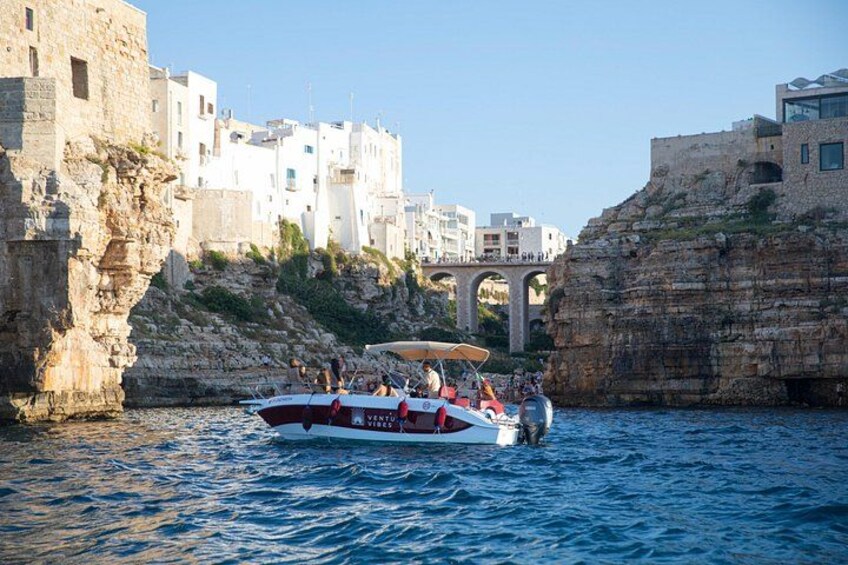 A boat with passengers on a rocky waterfront, a bridge, and buildings in the background. 4