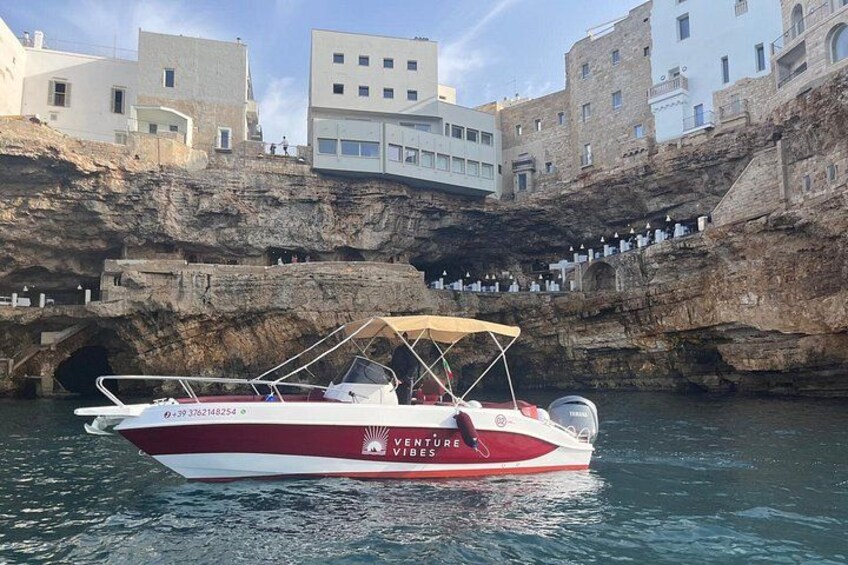 A boat named 'Venture Vibes' docked at a rocky waterfront with buildings in the background. 1