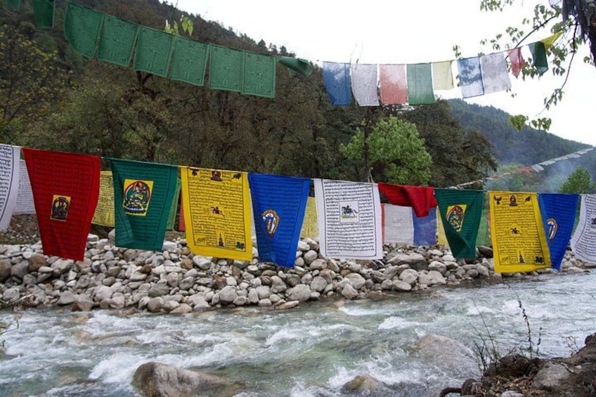 A river with flowing water, a rocky shore, and colorful prayer flags. 2