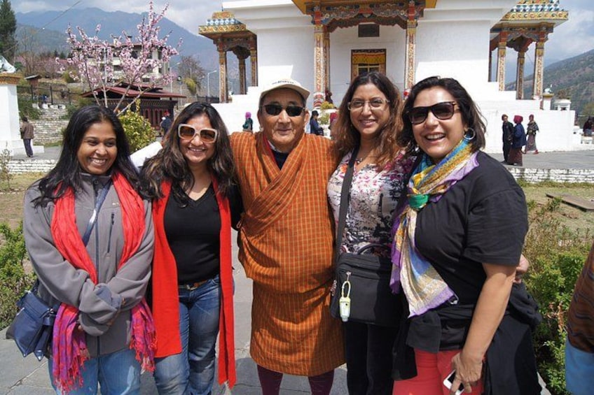 A group of people posing in front of a white building with traditional architecture, surrounded by greenery and mountains in the background. 4