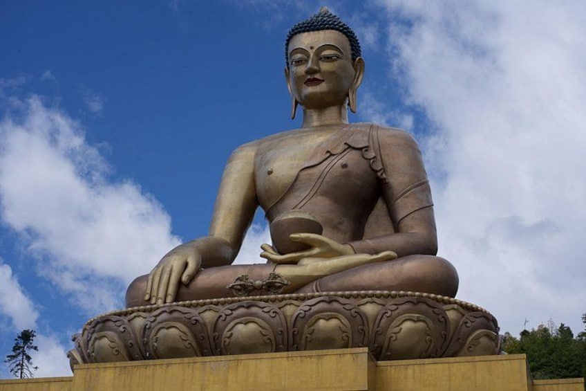 A large seated Buddha statue with intricate carvings on the base, set against a clear blue sky. 1