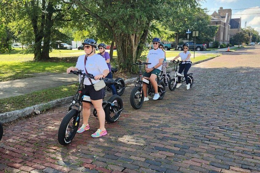 A group of people riding electric bikes on a brick pathway. 3