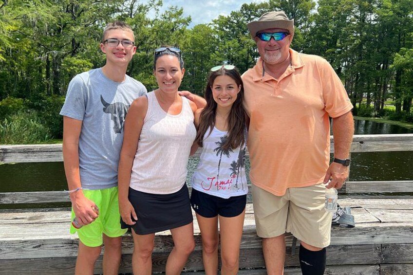 A group of people standing on a wooden bridge with a body of water and greenery in the background. 5