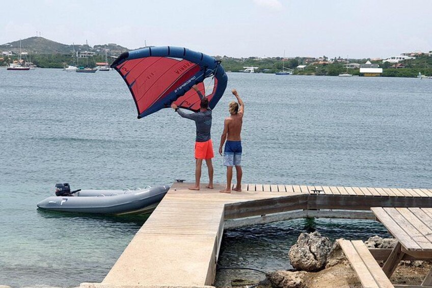 Two people on a dock with a parasail, a boat, and a rocky shoreline in the background. 5