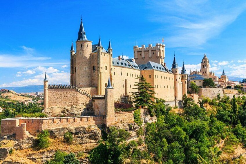 Un castillo histórico con múltiples torres, rodeado por una muralla fortificada y abundante vegetación. 5