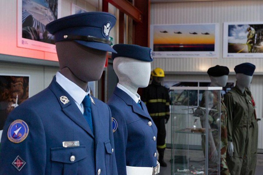 Des mannequins vêtus d’uniformes militaires, dont un uniforme de pilote et un uniforme de pompier, sont exposés dans un musée, avec des tableaux encadrés accrochés aux murs. 2