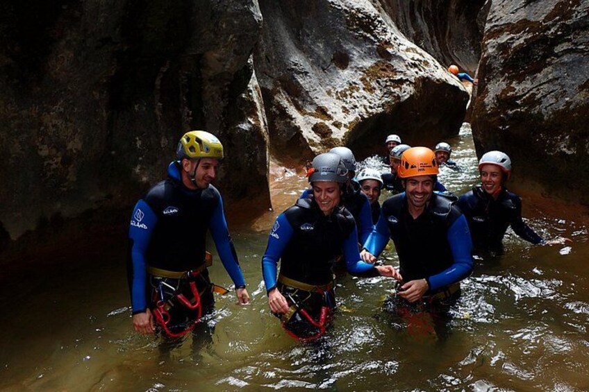 Un grupo de personas con trajes y cascos de neopreno vadean por un estrecho canal acuático rodeado de terreno rocoso. 1