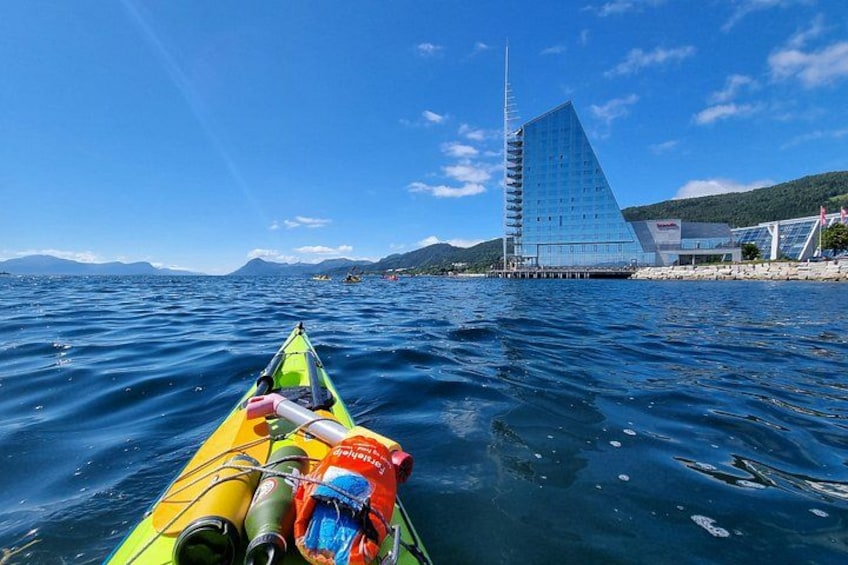 A kayak on calm water, a modern building with a unique shape, and distant mountains. 3