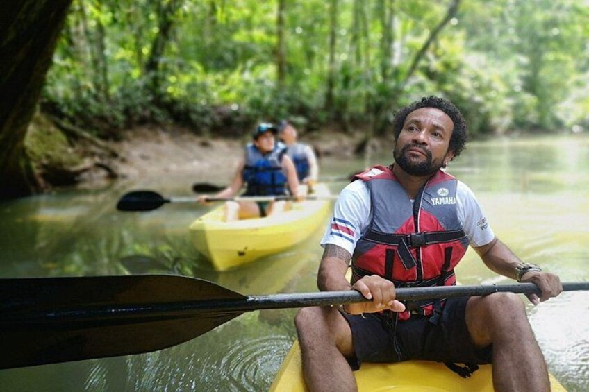 A person in a kayak on a river surrounded by greenery. 1