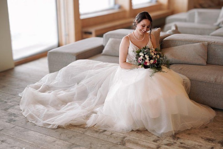 A person in a white wedding dress sitting on a couch with a bouquet. 5
