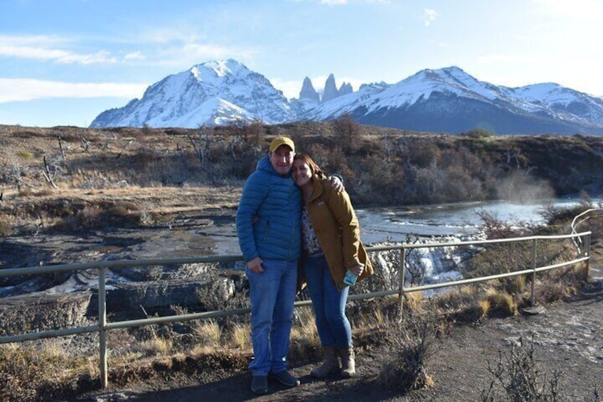Two people standing by a railing with a river and snow-capped mountains in the background. 4