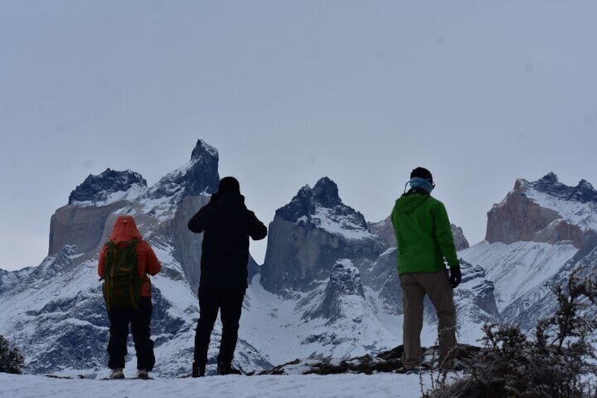 Three people standing on a snowy mountain peak, overlooking rugged, snow-covered mountains. 1