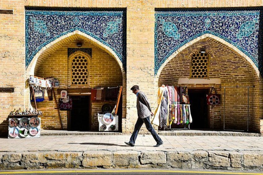 Una calle con una persona caminando, un puesto de mercado con productos y un edificio con detalles en azulejos. 5