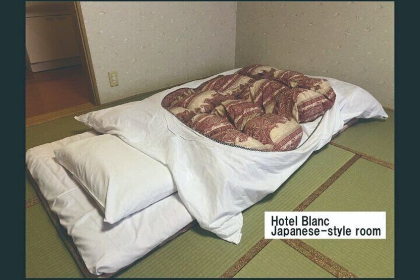 A Japanese-style room with tatami mats, a low bed with a patterned blanket, and white pillows. 5
