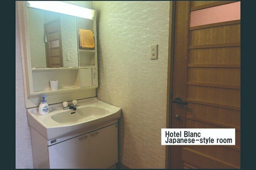A Japanese-style hotel room with a sink, mirror, and wooden door. 4