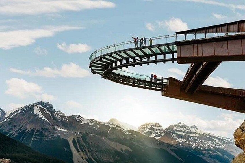 A glass bridge with people walking over it, surrounded by mountains and a clear sky. 1