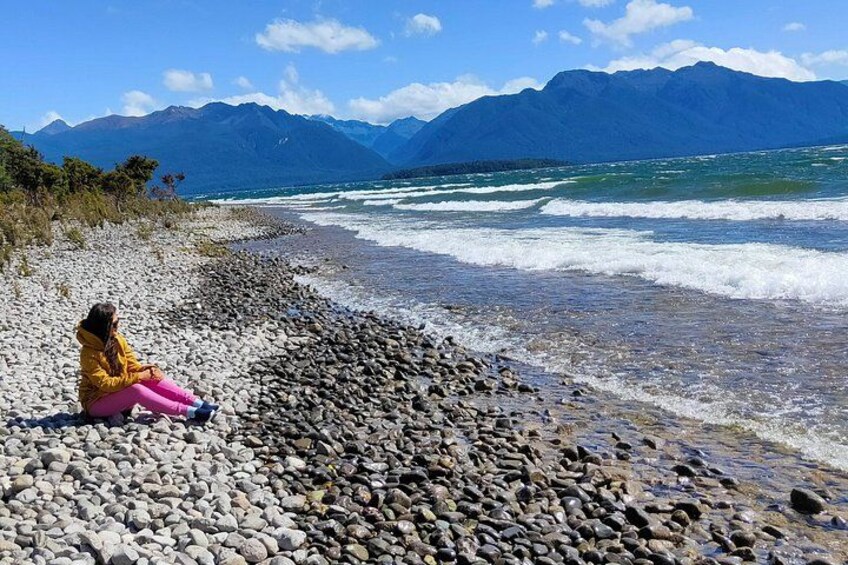 En person sitter på en stenig strand med berg i bakgrunden. 1