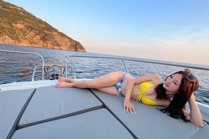 A person lying on a boat with a body of water and a cliff in the background. 4