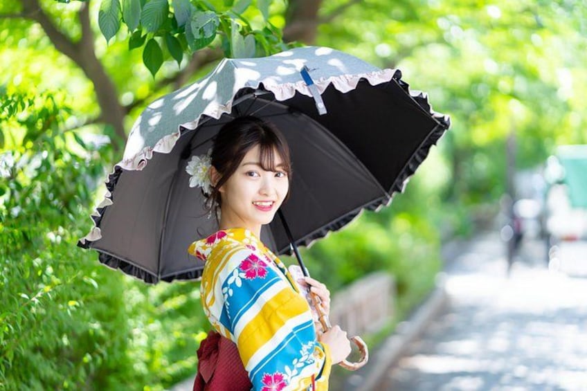 A person in a colorful kimono holding a black umbrella, standing on a tree-lined path. 3