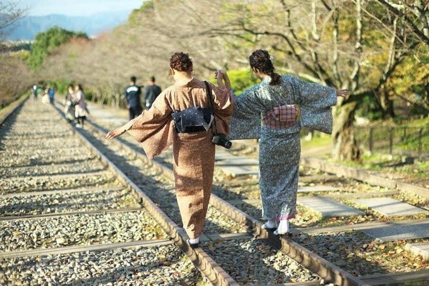 Two people in traditional Japanese attire walking along a railway track. 4