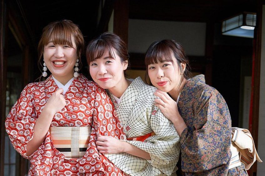 Three individuals wearing traditional Japanese kimonos, standing in front of a wooden structure. 2