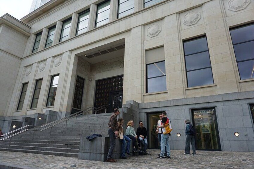 A group of people standing outside a building with large windows and a set of stairs leading up to the entrance. 3