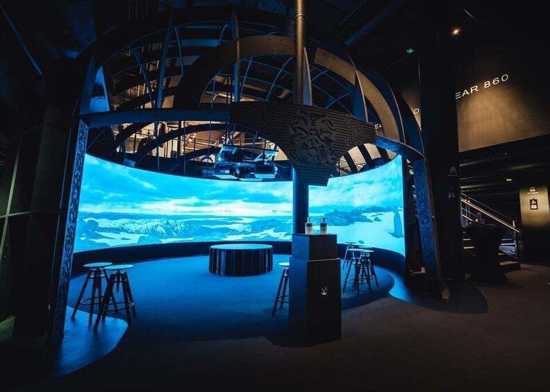 Un interior futurista con una gran pantalla digital, una zona de estar circular y una escalera. 1