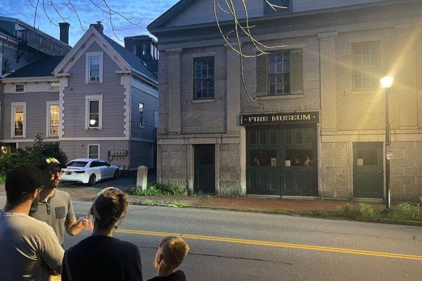 A street with a building labeled 'Fire Museum' and a white car parked on the side. 5