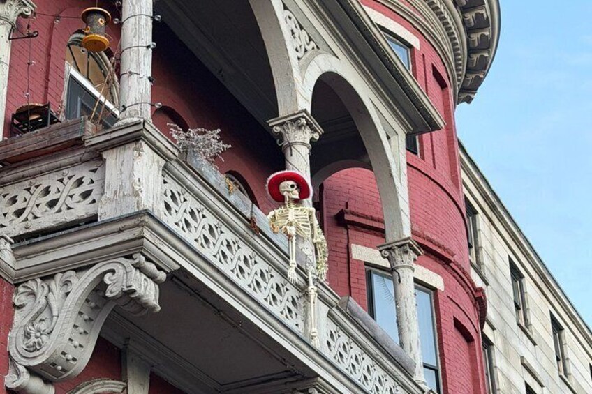 Fachada de edificio con detalles arquitectónicos ornamentales, incluyendo un balcón con una figura de esqueleto y un sombrero rojo. 5