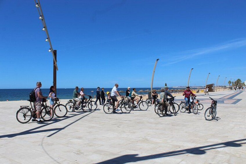A group of people riding bicycles along a coastal promenade with a clear sky. 1