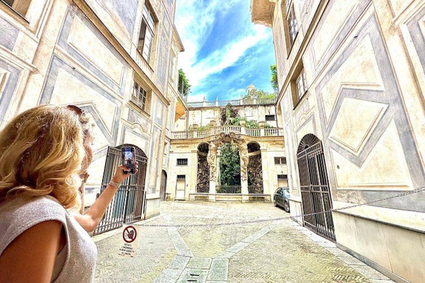 A woman taking a photo of a historic building with ornate architecture and a gated entrance. 5