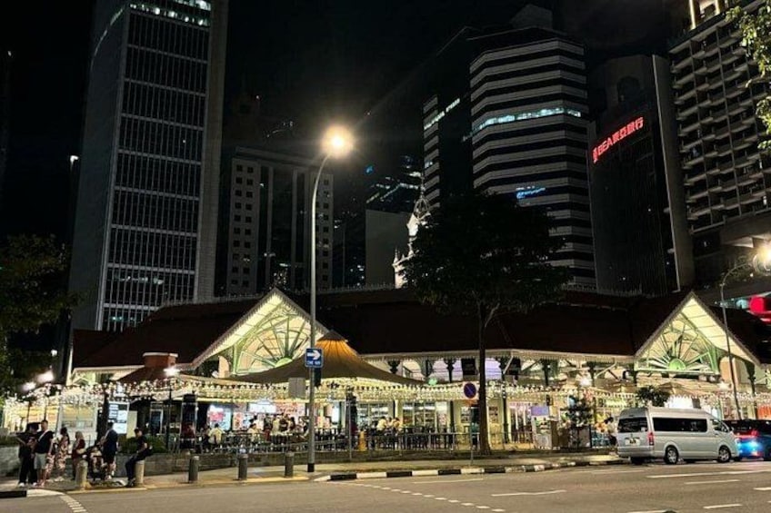 A brightly lit building with a distinctive roof structure, a street with a van, and modern high-rise buildings in the background. 2