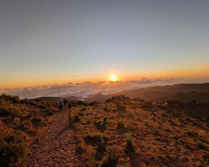 A sunrise over a mountainous landscape with a winding path leading to a group of people on a hill. 5