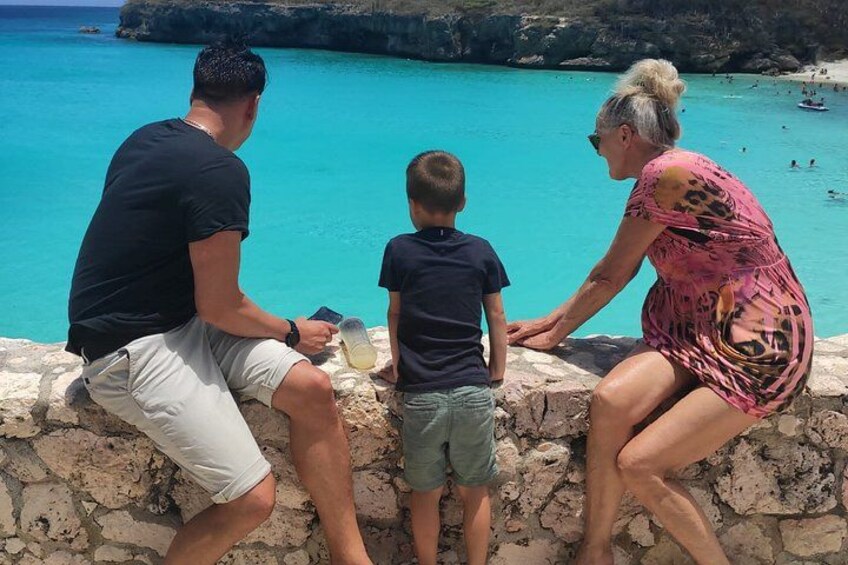En familj på tre personer vid ett turkosblått hav med en klippig kustlinje. 3