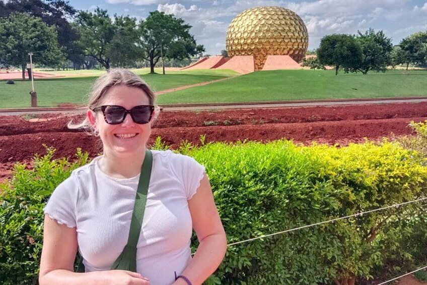 A person standing in front of a green hedge with a large spherical structure in the background. 1