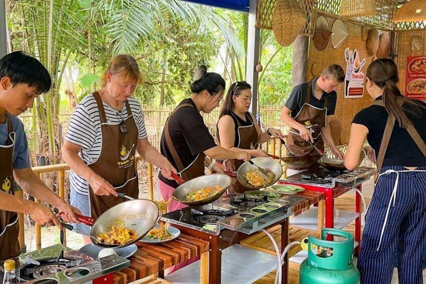 A group of people cooking outdoors, with a gas stove and cooking utensils on a wooden table. 1