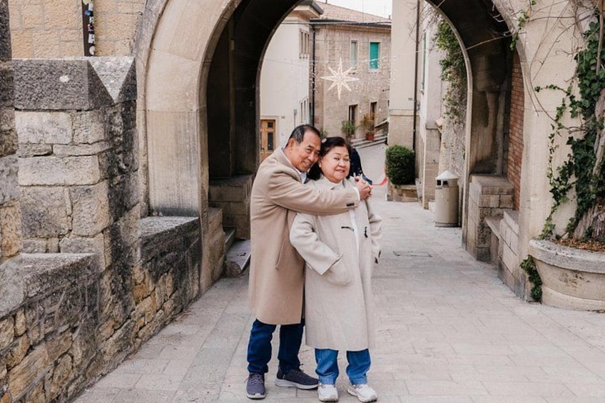 A narrow alleyway with stone walls, an archway, and a person in a coat hugging another person. 5