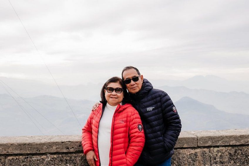 Two people standing on a ledge with a mountainous landscape in the background. 4