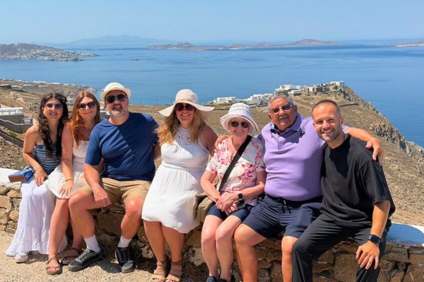 A group of people sitting on a stone ledge overlooking a coastal landscape with buildings and the sea in the background. 5