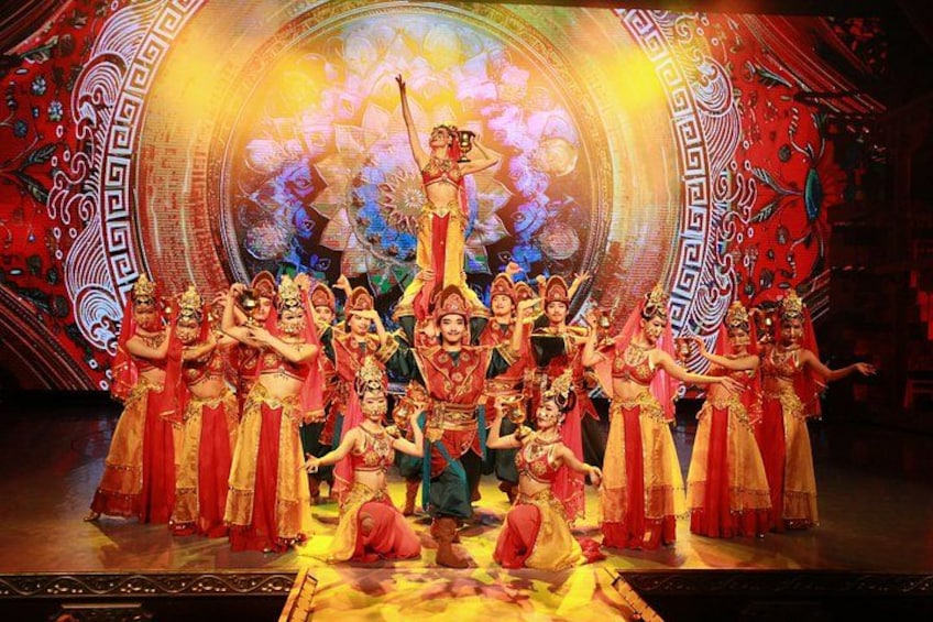 A group of performers in traditional costumes on a stage with a large, ornate backdrop. 3