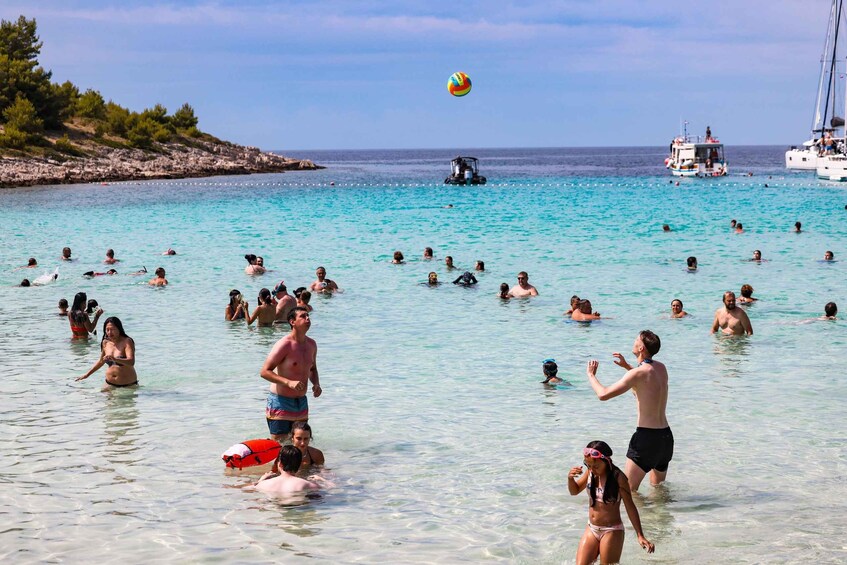 A crowded beach with people swimming and playing volleyball. 2