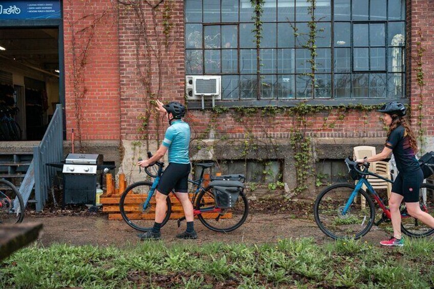 Two cyclists on a path with bicycles parked against a brick building. 2