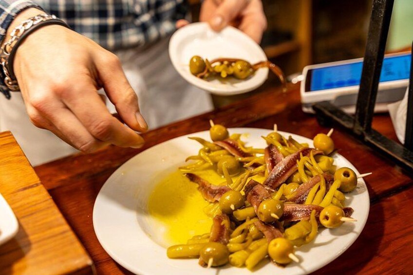 A person preparing a dish with olives and meat on a plate. 3