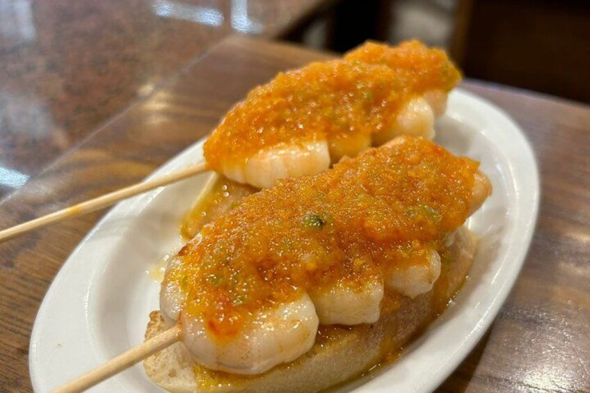 Deux morceaux de poisson, enfilés sur une brochette, sont présentés sur une assiette blanche et recouverts d’une garniture dorée et brune. 4