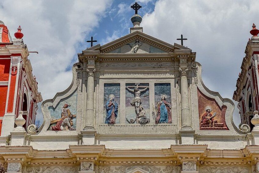 Een gevel van een kerk, versierd met religieuze schilderijen en een kruis bovenop. 2