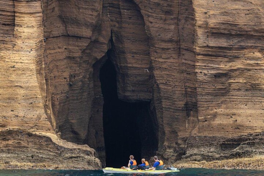 A large rock formation with a cave entrance, a person in a kayak, and two individuals on a raft. 4