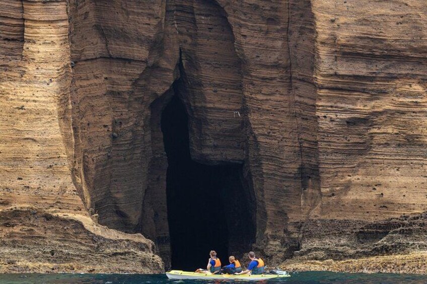 Una gran formación rocosa con la entrada de una cueva, una persona en kayak y dos personas en una balsa. 3